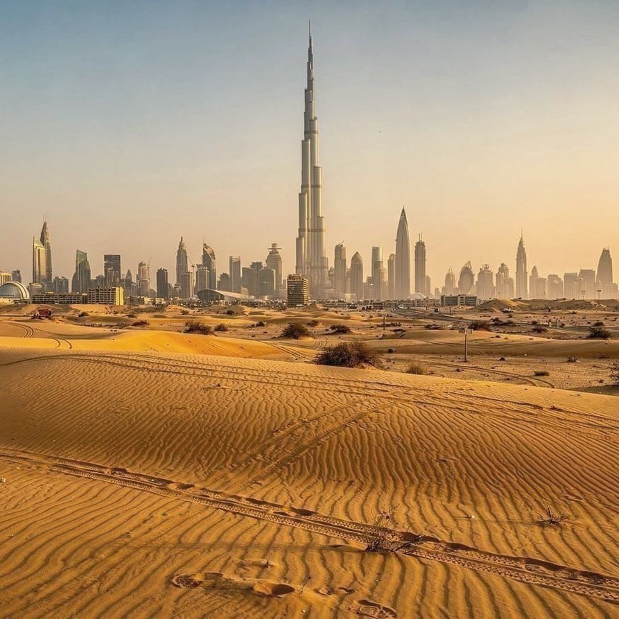 The Dubai skyline and the Burj Khalifa seen across desert dunes in golden light