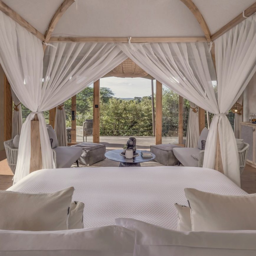 A canopy bed in a tented suite at JW Marriott Masai Mara Lodge, open to the deck and the bush beyond