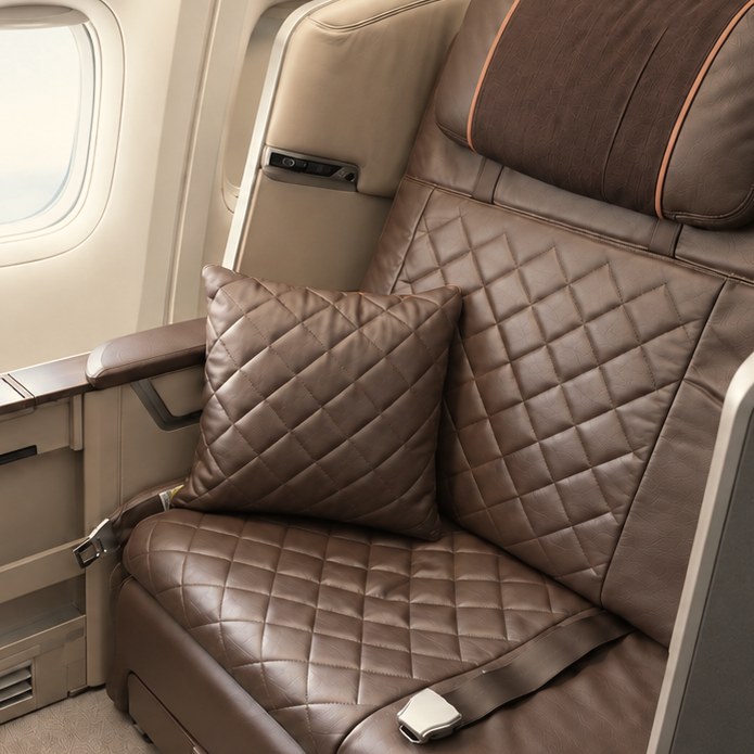 A Singapore Airlines first class seat in brown quilted leather beside a window, daylight